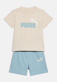 Μπεζ μπλουζάκι για νήπια με κοντά μανίκια και μπλε λογότυπο "PUMA" και ανοιχτό μπλε σορτς με ελαστική μέση και λευκό λογότυπο "PUMA" στο αριστερό πόδι.