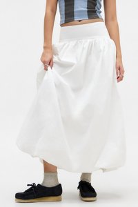 Gonna lunga bianca con vita arricciata, realizzata in tessuto leggero. Presenta una texture solida e liscia ed è indossata con scarpe nere e calzini grigi.