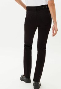 Vaqueros de mezclilla negros con un corte ajustado, que presentan bolsillos traseros, pasadores para cinturón y una textura suave. Combinados con zapatos de plataforma negros.