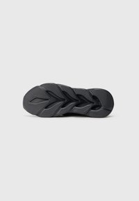 Talpă de sneaker negru cu un model texturat, inspirat de frunze, pe un fundal gri deschis plain.