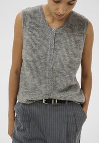 Harmaa neulemainen hihaton paita, jossa on pyöreä kaula-aukko ja viisi napin suljinta. Teksturoitu kangas, jossa on hienovaraisia sävyvaihteluita.