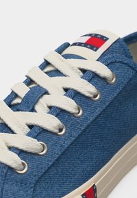 Μπλε τζιν αθλητικό παπούτσι με λευκά κορδόνια και λογότυπο Tommy Jeans στη γλώσσα και στη σόλα, κοντινή όψη.