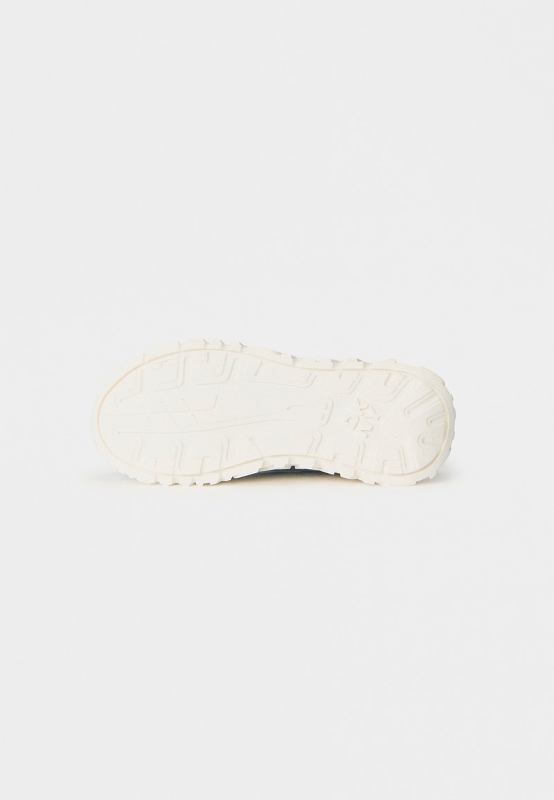 Suola di scarpa bianca con profonde scanalature e un motivo testurizzato, fotografata su uno sfondo bianco uniforme.