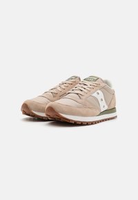 Beige joggesko med en blanding av semsket skinn og stoff, med hvite detaljer, grønn logo, snøring og strukturert gummielast.