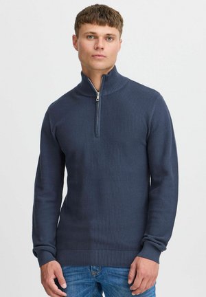 Suéter de cuello con cremallera en oscuridad marina, fabricado con un tejido texturizado y tejido, con puños y dobladillo de canalé. Presenta un cuello con media cremallera para un estilo ajustable.