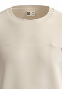 Lichtbeige shirt met korte mouwen en een ronde halslijn, geperforeerde stof, horizontale naaddetails en een klein zakje met hardwareaccent.