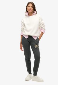 Biała bluza zakładana na różową koszulę z kołnierzykiem, połączona z szarymi spodniami dresowymi z złotym napisem. Całość dopełniają białe trampki.