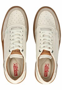 Sneaker bianchi in pelle con texture perforata, dettagli in suede beige e suole in gomma marrone. I lacci sono bianchi; l'interno presenta un logo rosso.
