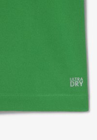 Polo verde con un tessuto testurizzato. Presenta la scritta "ULTRA DRY" stampata in bianco vicino all'orlo. Vestibilità classica e maniche corte.