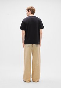 Črna bombažna majica s kratkimi rokavi, kombinirana s svetlimi širokimi hlačami, ki imajo minimalne detajle in gladko teksturo.