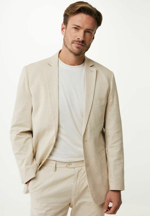 Beige Leinenblazer mit einem einzigen Knopf, Reverskragen und Brusttasche, über einem weißen T-Shirt getragen. Lässiger Schnitt mit leichter Textur.