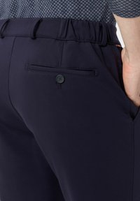 Pantalons à taille élastique bleu marine, avec une poche arrière à bouton, texture lisse et coupe ajustée.