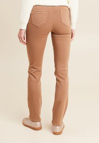 Pantaloni marroni aderenti in tessuto elasticizzato, con vita media, gambe affusolate, due tasche posteriori e dettagli di cucitura minimali.