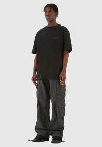 Sort oversized t-shirt med korte ærmer og logo foran, parret med mørkegrå cargo-bukser med flere lommer og justerbare ben.
