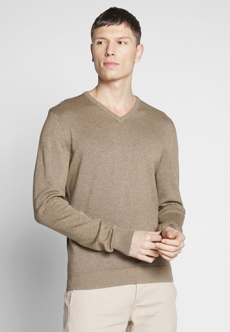 Suéter marrón de cuello en V hecho de tela ligera, con mangas largas y puños y dobladillo acanalados. Llevado con pantalones beige claro.