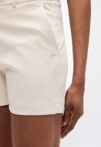 Ανοιχτό μπεζ σορτσάκι κατασκευασμένο από απαλό ύφασμα. Διαθέτει πλαϊνές τσέπες και διακριτικό ανάγλυφο λογότυπο στο αριστερό πόδι. Καλοραμμένη εφαρμογή με διπλωμένο τελείωμα.