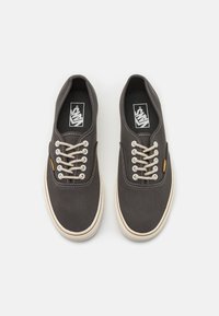 Kaks osat tummaharmaita Vans-tennareita, joissa on valkoiset pohjat ja beige narut, kuvattuna ylhäältä yksinkertaisella valkoisella taustalla.