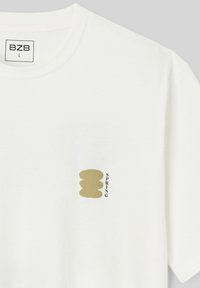 T-shirt blanc avec encolure ronde, étiquette de taille "BZB L" et petite forme abstraite dorée avec le mot "SPRING" imprimé verticalement sur la poitrine.