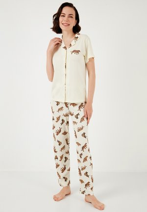 Kremasta kratka majica s dugmadi za pidžamu s izvezenim leopard uzorcima, u paru s bijelim hlačama koje imaju smeđi leopard uzorak.