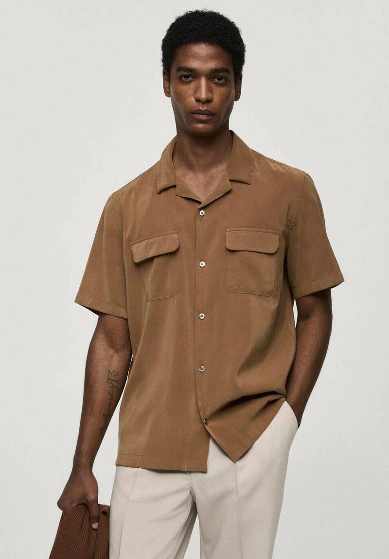 Korte mouwen bruin shirt van gladde stof, met een kraag, twee borstzakken en knoopsluiting, gecombineerd met lichte broek.