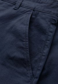 Gros plan sur un tissu bleu foncé montrant une poche avant et les détails de couture d'un pantalon ou d'un short.