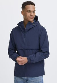 Navy hooded jacket with a zip closure, elastic cuffs, and a lightweight, textured fabric. Contains a front pocket and adjustable hood.