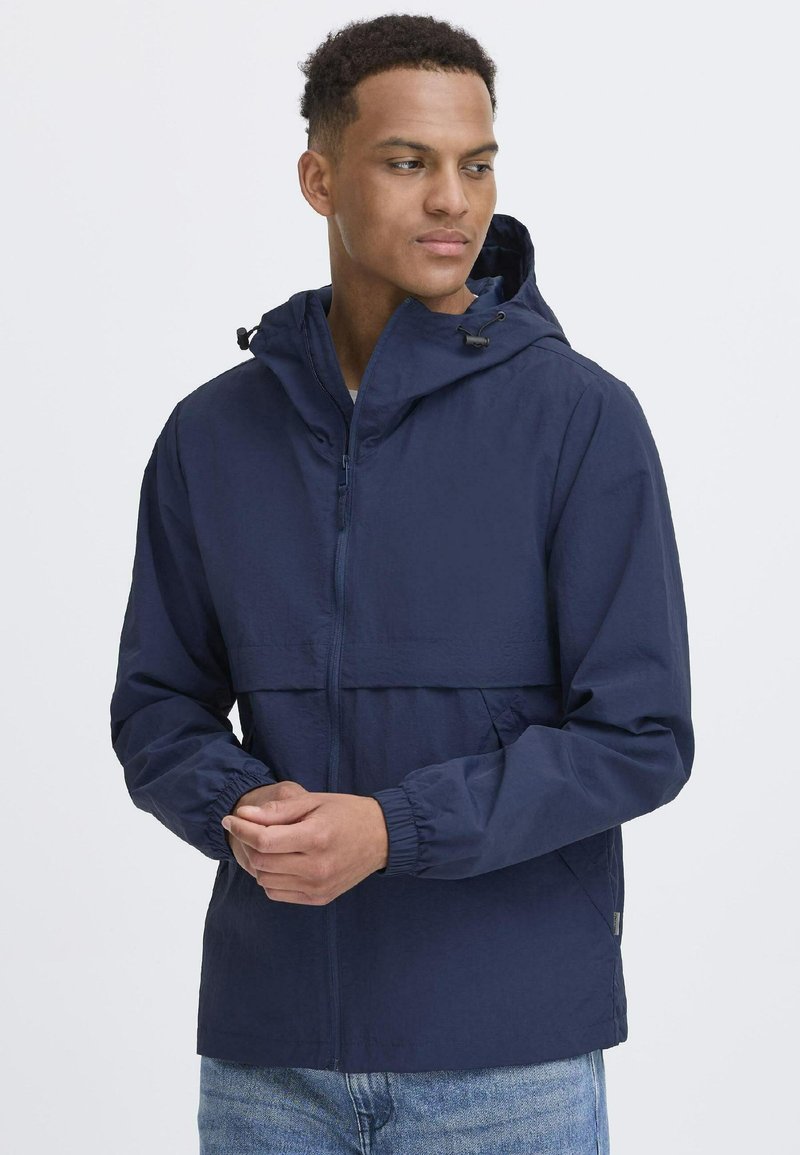 Navy hooded jacket with a zip closure, elastic cuffs, and a lightweight, textured fabric. Contains a front pocket and adjustable hood.