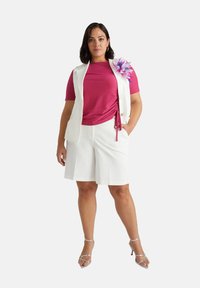 Canotta bianca senza maniche, top rosa a maniche corte con dettagli plissettati, pantaloni corti bianchi e tacchi metallici con cinturini. Nota accentuazione floreale sulla canotta.
