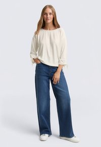 Helebeež, pika varrukaga pluus paadi kaelusega ja seotud detailidega varrukatel, sobitatud laia säärega siniste teksade ja valgete vabaajajalatsitega.