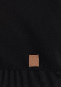 Maglione nero con texture a coste e una piccola etichetta in pelle marrone con logo impresso in vita. Materiale morbido, design minimalista.