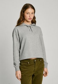 Grå cropped hettegenser med snor, lange ermer, og en subtil logo. Kombinert med olivengrønne, tettsittende bukser med frontlommer.