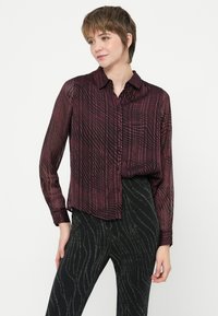 Camicia bottone a maniche lunghe color marrone scuro con un motivo a righe texturizzato. Il tessuto appare leggero e leggermente trasparente.
