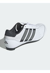 Bílé tenisky s černým podpatkem, černou podešví, třemi černými pruhy po straně, perforovanou špičkou a bílými tkaničkami.