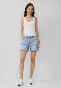 Lichte blauwe denimshorts met opgerolde pijpen, voorzien van voorzakken en een knoopsluiting. Gecombineerd met een wit tanktop en sneakers.