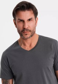 Šedé tričko s krátkým rukávem a véčkovým výstřihem. Měkká textura, přiléhavý střih, minimální švy a čistý výstřih. Žádné viditelné vzory nebo akcenty.