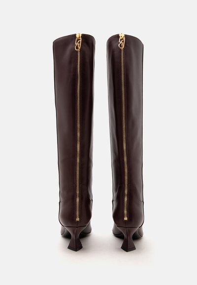 Paire de bottes en cuir marron foncé montant jusqu'au genou avec des fermetures éclair dorées verticales au dos et des talons bas.