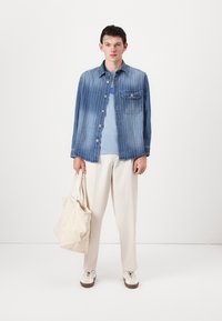Denim jacket with vertical white stripes, blue t-shirt, cream pants, and a cream tote bag. Model wearing white sneakers with brown soles.
