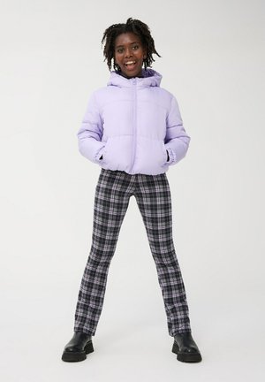 Giacca a vento viola chiaro con cappuccio, pantaloni a quadri neri e viola, e stivali neri chunky, caratterizzati da una texture morbida e una vestibilità rilassata.