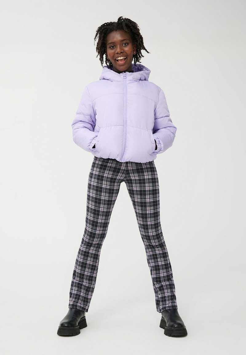 Giacca a vento viola chiaro con cappuccio, pantaloni a quadri neri e viola, e stivali neri chunky, caratterizzati da una texture morbida e una vestibilità rilassata.