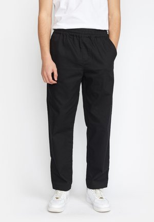 Zwarte broek met elastische taille, zijzakken, rechte snit en een gladde textuur. Gecombineerd met witte sneakers.