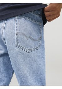 Ljusblå denimjeans med en lätt blekt struktur, som har en distinkt böjd sömnadsmönster på bakfickan.
