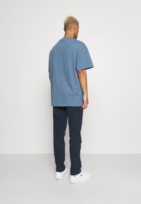 Camiseta de algodón azul de gran tamaño con mangas cortas, combinada con pantalones oscuros y zapatillas blancas. Diseño sencillo, sin patrones o logotipos visibles.