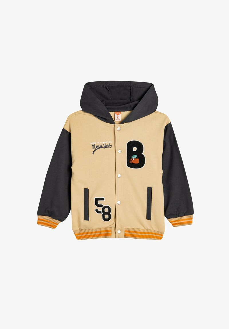 Beige og sort hættejakke med trykknapper. Har broderet tekst, numre og et grafik på forsiden. Ribbede orange manchetter.