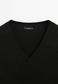 Pull col en V noir en laine douce, avec poignets et ourlet côtelés, et une petite étiquette à l'intérieur indiquant la marque et l'origine.