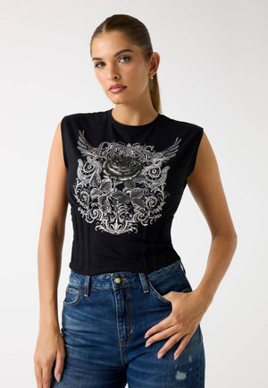 Top negro sin mangas con un diseño gráfico que presenta una rosa y patrones ornamentales, combinado con jeans de tiro alto azules.