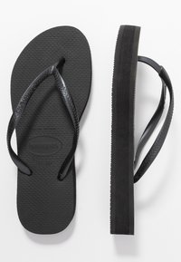Mustat kumiset flip-flopit, joissa on teksturoitu pohja, V-muotoiset hihnat ja litteä pohja. Pohjassa on lievää kohotusta ja sileä reuna.