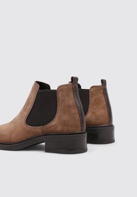 Bottines en suede marron avec des panneaux latéraux élastiques noirs, des accents en cuir texturé marron et un petit talon carré.