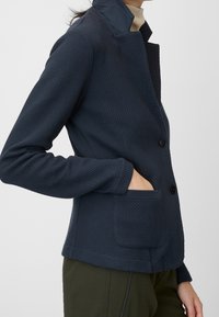 Blazer texturizado de color azul marino con cuello, dos botones y bolsillos laterales. Fabricado con material suave, presenta una silueta ajustada.