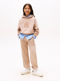 Bež bombažni pulover s kapuco z logotipom, kombiniran s črtasto modro srajco in ujemajočimi se zoženimi trenirkami, dopolnjen z belimi supergami.