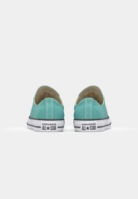 Turquoise canvas slip-on sneakers with white rubber soles, featuring "CONVERSE ALL STAR" branding and black striped accents on the sole.